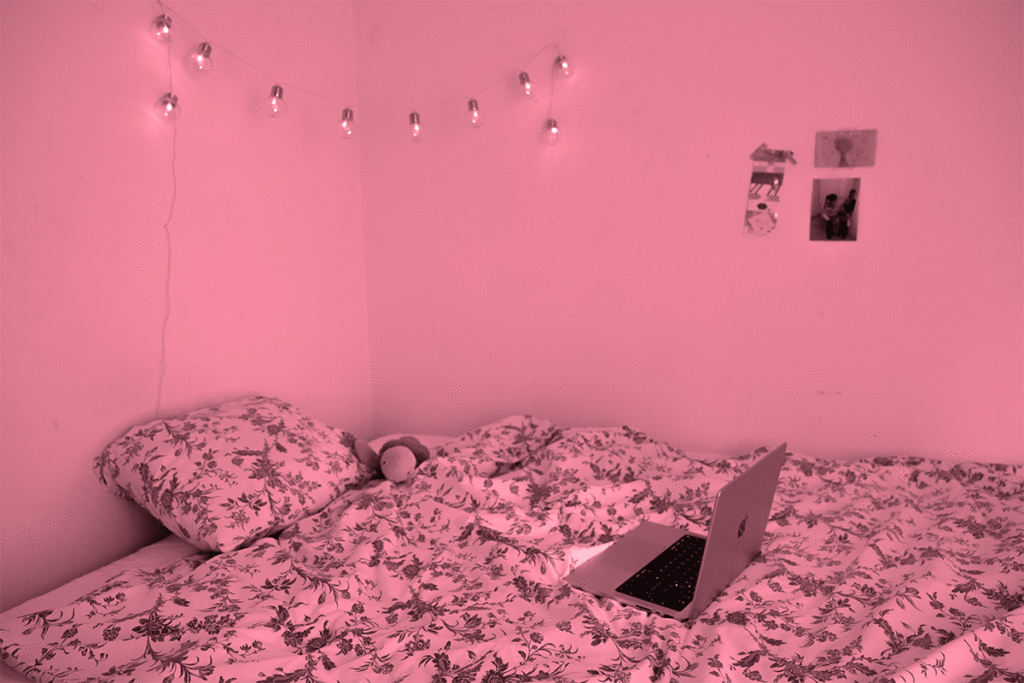 Cozy bedroom with floral bedding, a laptop on the bed, and string lights on the wall.