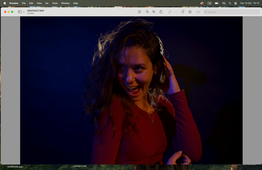 A woman in a red top dancing and laughing during a photoshoot, illuminated by warm and cool studio lights.
